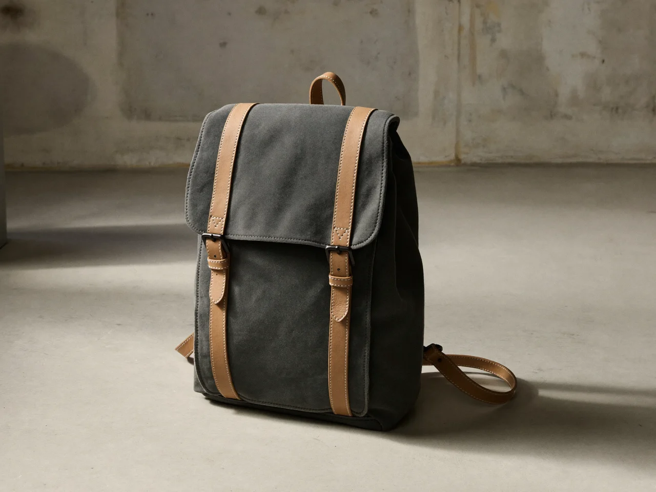 Dunkler Canvas-Stadtrucksack mit Lederriemen vor einer hellen Atelierwand