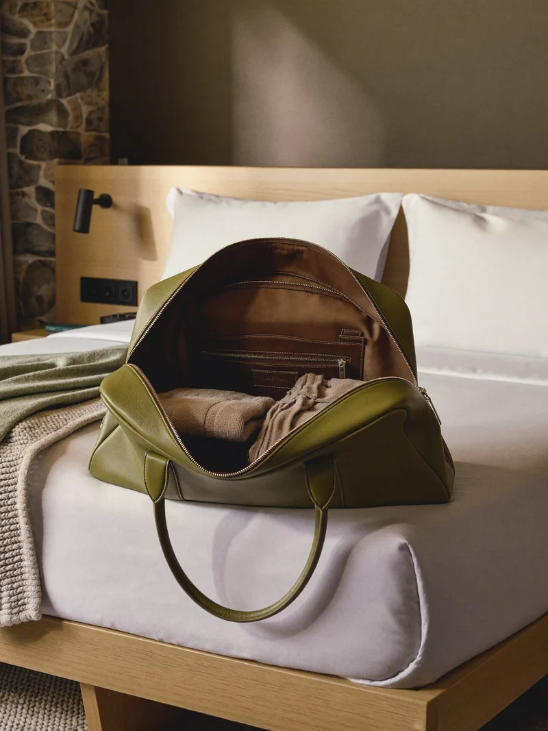 Olivgrüner Weekender, geöffnet auf einem Bett im Berghotelzimmer