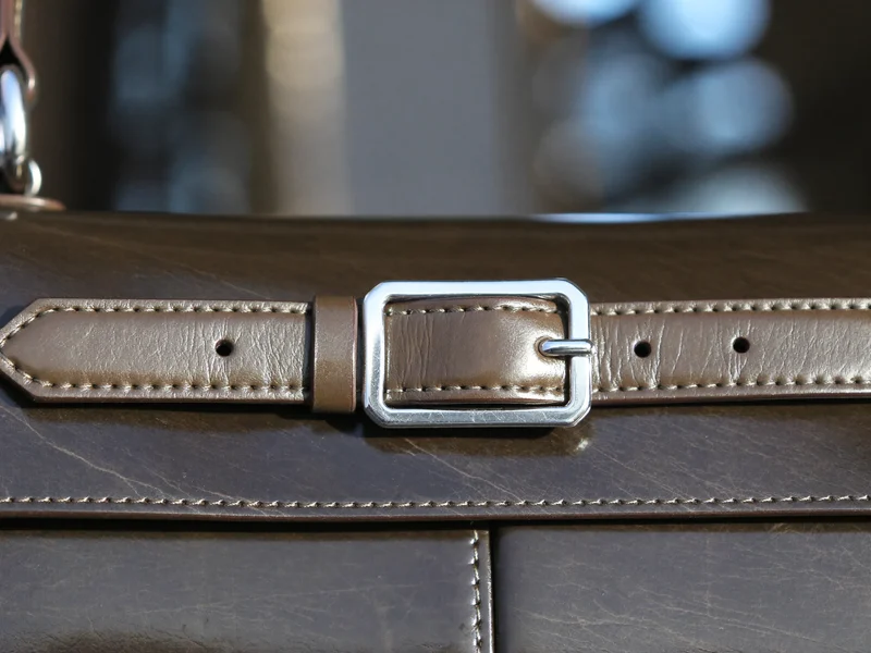 Nahaufnahme einer handgenähten Taschennaht mit Metallschnalle auf Leder